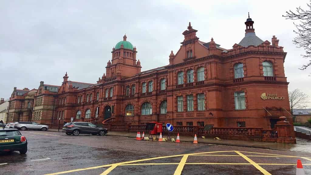 The ornate, historic, multi-story Hotel Indigo building in Durham, constructed of deep red brick with arched windows and a green-domed turret.