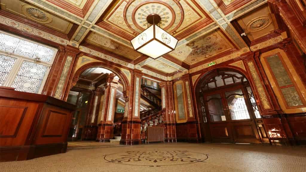 The Preserved Grandeur of the Old Shire Hall Lobby A view of the highly decorative entrance hall of the Old Shire Hall, featuring polished red and cream tiled walls, a patterned mosaic floor, a coffered ceiling with a central lantern, and archways leading to the preserved grand staircase.