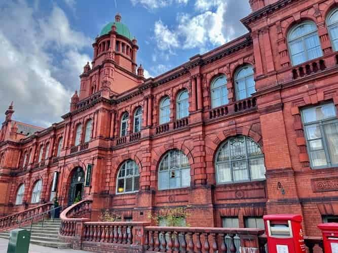 Exterior view of the Old Shire Hall, Durham (Hotel Indigo), a grand red-brick Baroque Revival building with a green-domed tower, arched windows, and a stone staircase leading to the main entrance.