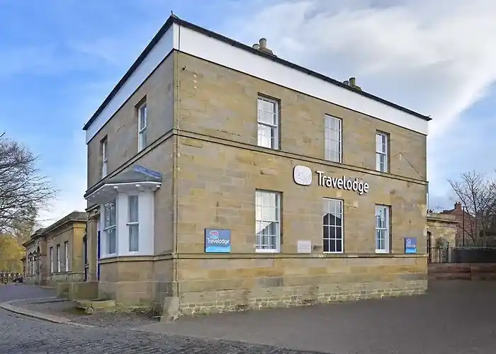 Durham Gilesgate Travelodge Hotel in Former Historic Stone Building Color photo of the Durham Gilesgate Travelodge, a two-story hotel in a historic, yellowish-brown stone building with a corner bay window. The white Travelodge logo is affixed to the stone facade.